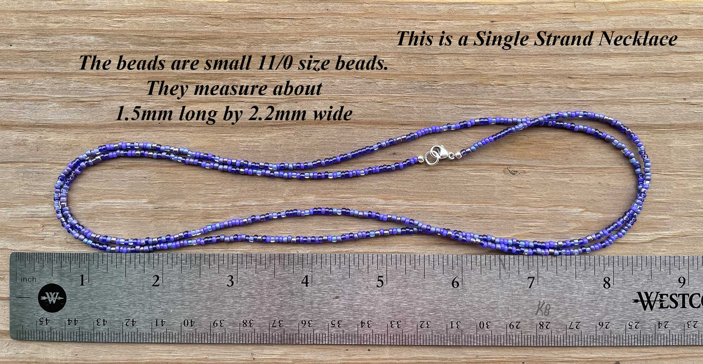 Single strand necklace with small beads on a wooden surface with a ruler for scale.