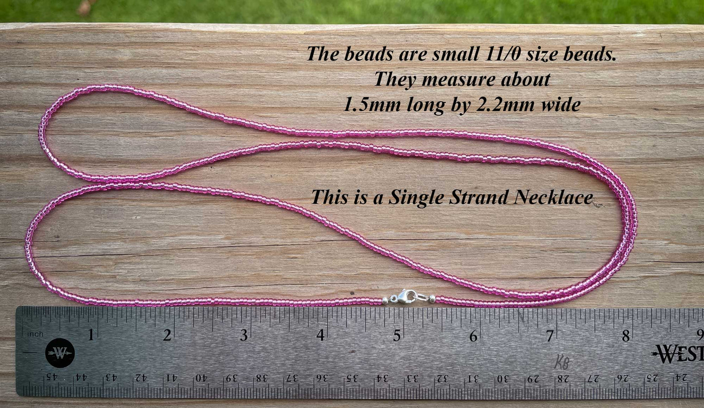 Pink single strand necklace with measurement text on a wooden surface