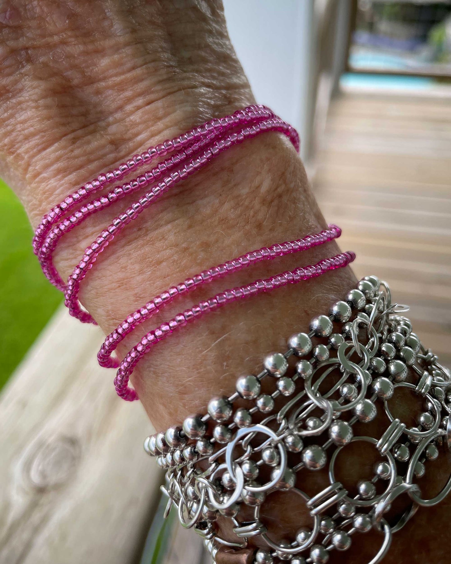 Close-up of a wrist wearing pink beaded bracelets and silver chain bracelets.