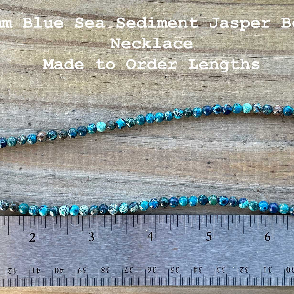 
                      
                        4mm Blue Sea Sediment Jasper Bead Necklace on a wooden surface with a ruler for scale.
                      
                    