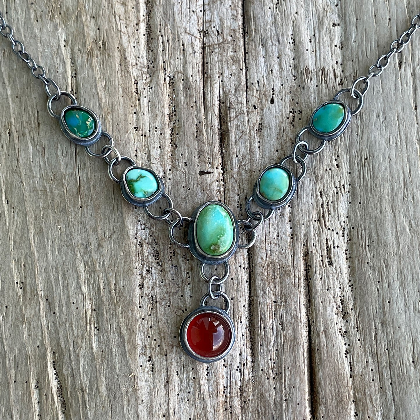 A detailed close-up of Sonoran turquoise and carnelian stones set in hand-worked fine silver, displayed against a rustic weathered wood background to show the natural stone character.