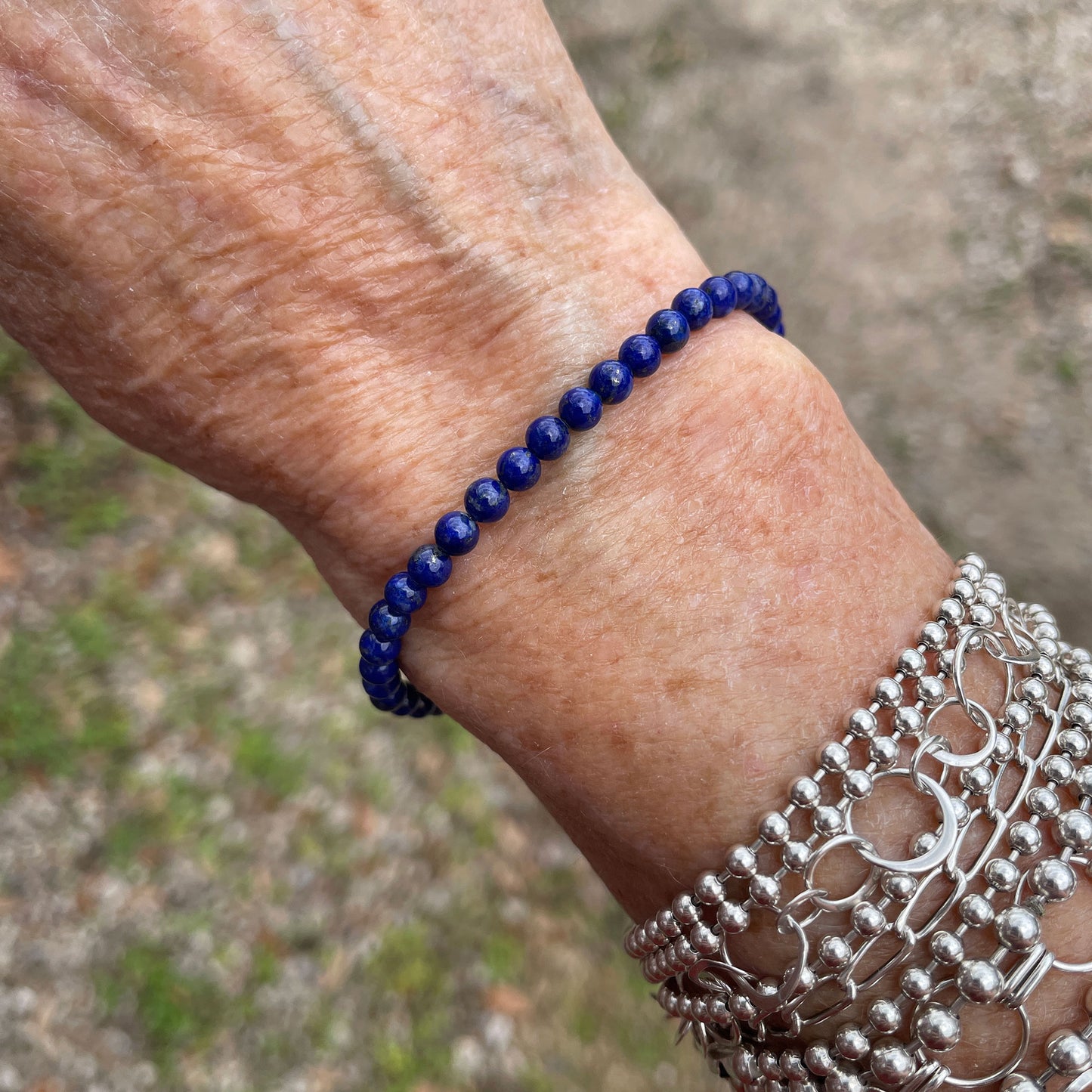 Close-up of a wrist wearing a blue Lapis beaded bracelet with a blurred natural background