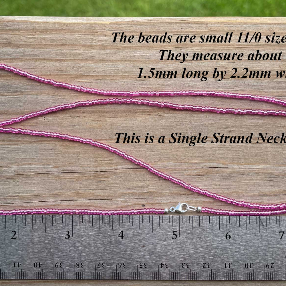 
                      
                        Pink single strand necklace with measurement text on a wooden surface
                      
                    