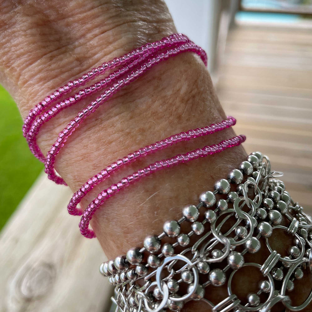 
                      
                        Close-up of a wrist wearing pink beaded bracelets and silver chain bracelets.
                      
                    