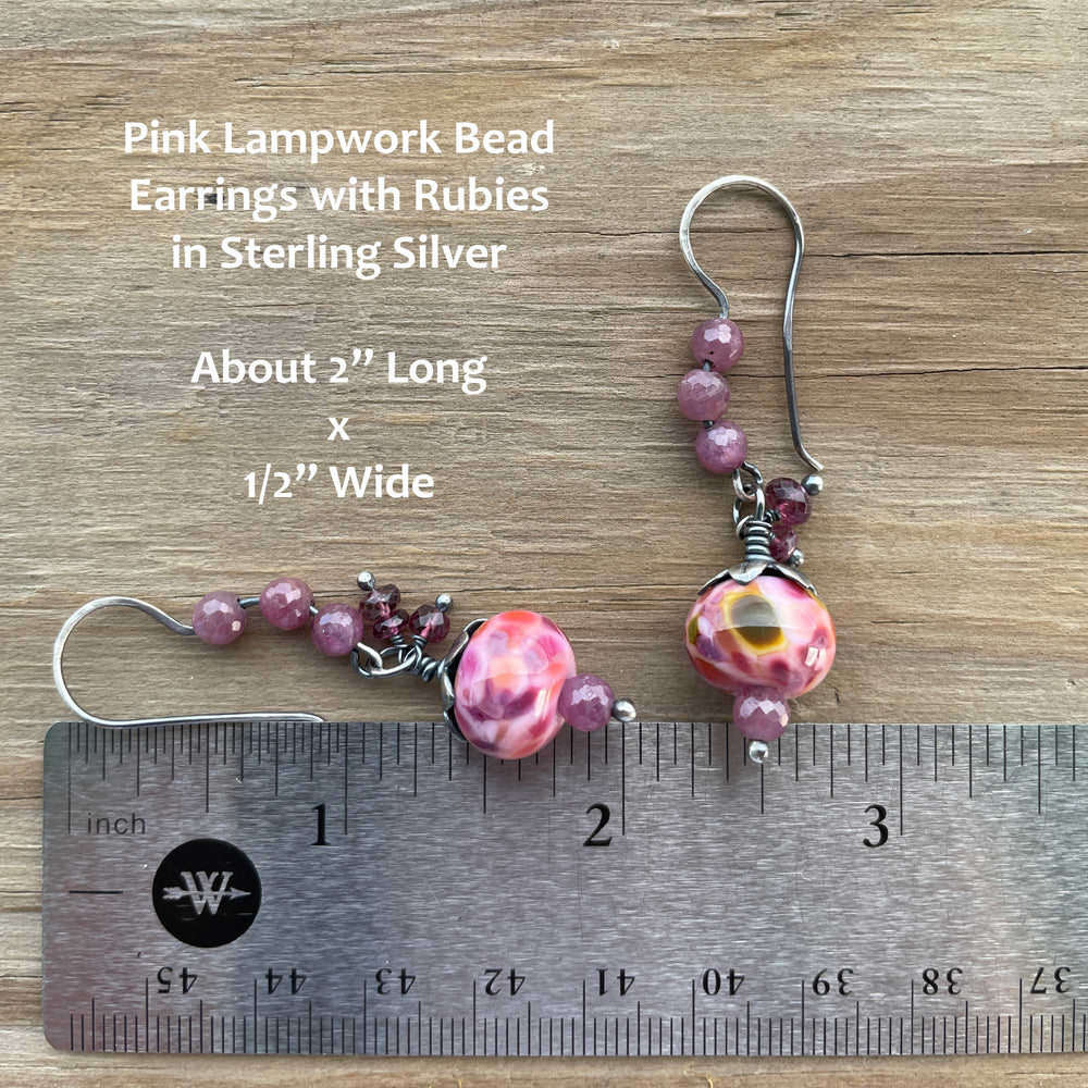 
                      
                        Pink lampwork bead earrings with rubies in sterling silver on a wooden surface with a ruler for scale.
                      
                    