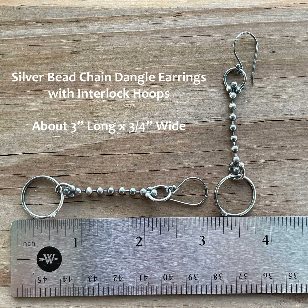
                      
                        Silver bead chain dangle earrings with interlock hoops on a wooden surface with a ruler for scale.
                      
                    