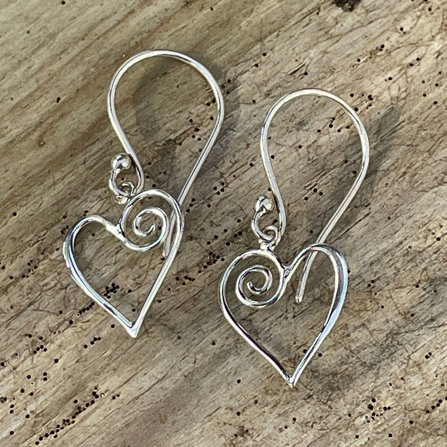 Silver heart-shaped earrings with swirl details on a wooden surface