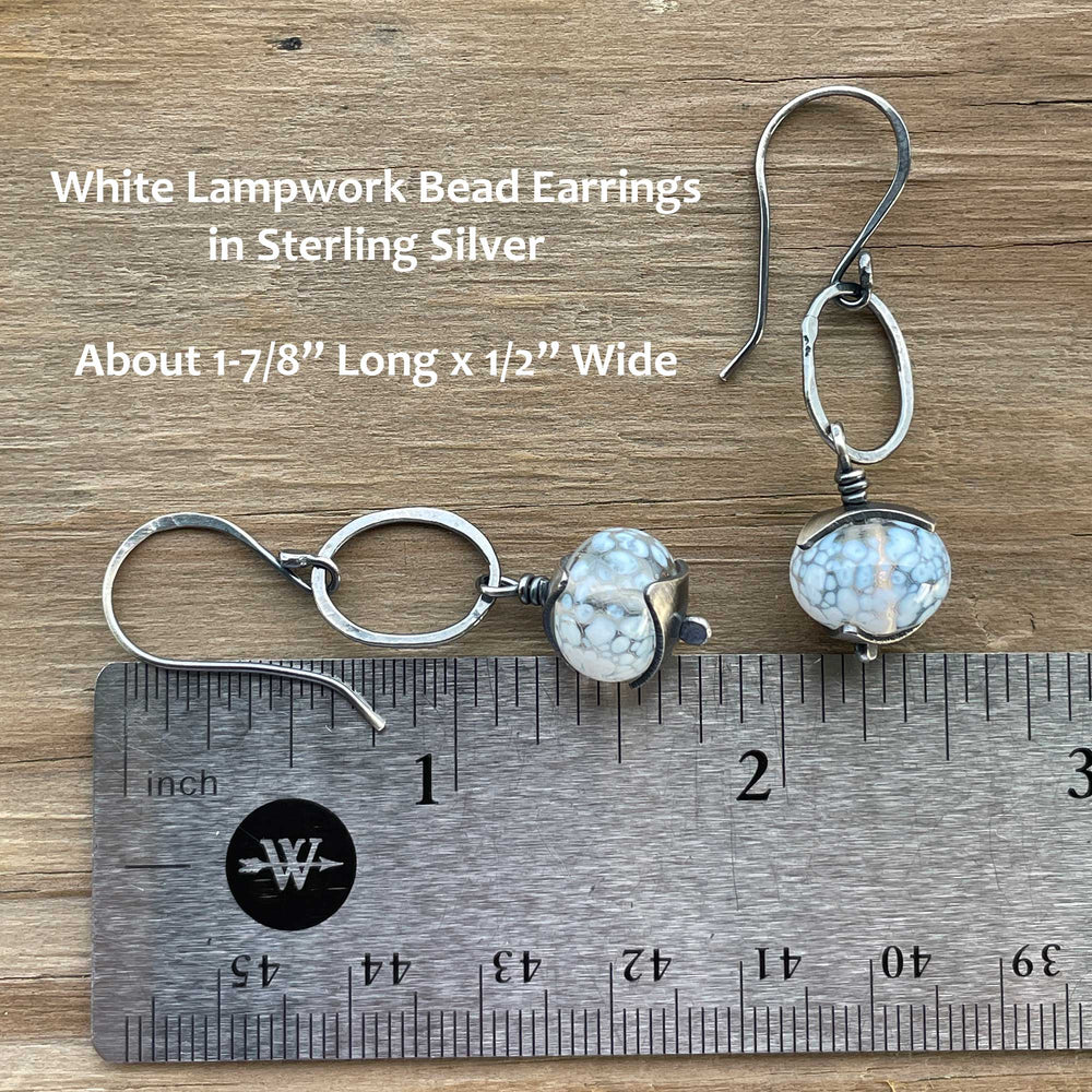 
                      
                        White lampwork bead earrings in sterling silver on a wooden surface with a ruler for scale.
                      
                    